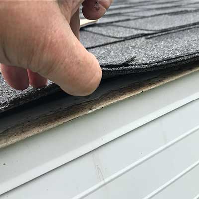 Close up of a hand lifting up a roof shingle to inspect it