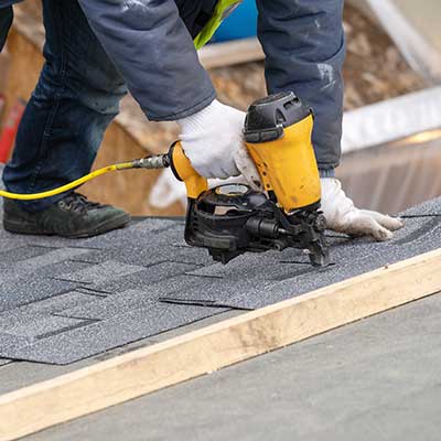 Roofer installing gray shingles on a newly constructed home with a nail gun