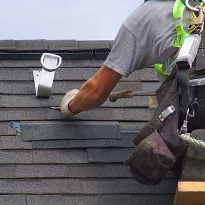 Roofer repairing some dark gray shingles on a residential roof that has suffered some damage